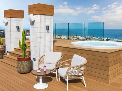 Dachterrasse mit Holzverkleidung, Whirlpool, zwei Stühlen und Tisch mit Getränken und Kakteen.