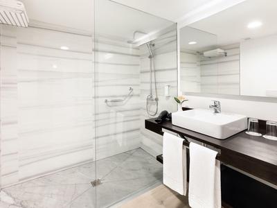 Modernes Hotelbadezimmer mit großer begehbarer Dusche und Waschbecken auf dunklem Holz.