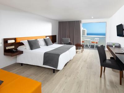 Modernes Hotelzimmer mit Doppelbett, Schreibtisch, Sitzecke und Blick auf das Meer.