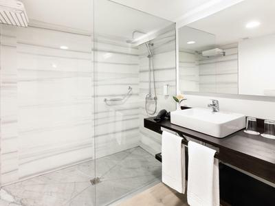 Modernes Hotelbadezimmer mit Dusche, großem Spiegel und Waschbecken auf dunklem Holz.