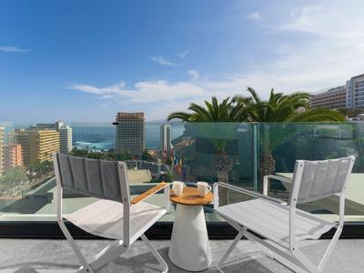 Balkon mit zwei weißen Sesseln, kleinem Tisch und Blick auf Stadt und Meer unter blauem Himmel.