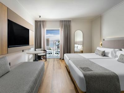 Modernes Hotelzimmer mit Doppelbett, Sofa, Fernseher und Balkon mit Meerblick.