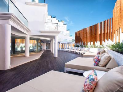 Moderne Terrasse mit weißen Loungemöbeln, Holzboden und dekorativen Kissen unter blauem Himmel.