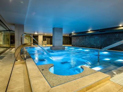 Moderner Innenpool mit blauer Beleuchtung, weißem Deck und glasierten Wänden bei Dämmerung.