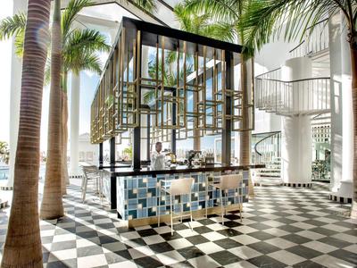 Moderner Barbereich mit Glasstruktur, Palmen und schwarz-weiß kariertem Boden in hellem Raum.