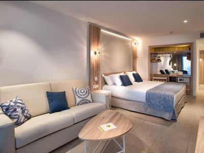 Modern eingerichtetes Hotelzimmer mit Doppelbett, Sofa, Holztisch und großer Spiegelwand.