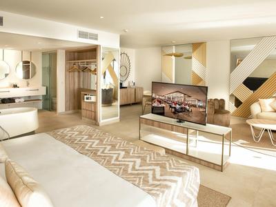 Helles Wohnzimmer mit beiger Polstermöbel, geometrischem Wanddesign und großem Flachbildschirm.