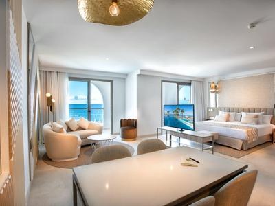 Helles Wohnzimmer mit großen Fenstern, cremefarbenen Möbeln und Blick auf das Meer.