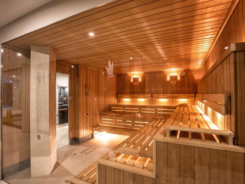 Innenraum einer modernen Sauna mit Holzverkleidung, Sitzbänken und warmem Licht.