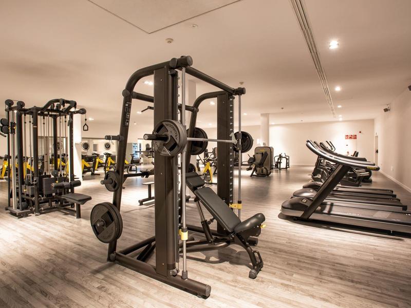 Moderner Fitnessraum mit Kraftgeräten, Hanteln, Laufbändern und hellem Holzboden.