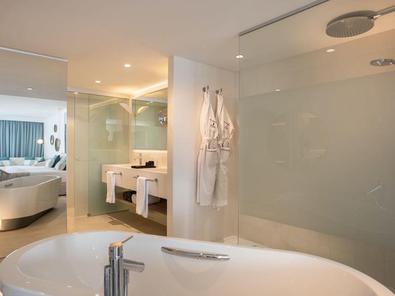 Moderne Badezimmergestaltung mit freistehender Badewanne, Glastrennwand und offenem Schlafzimmerblick.