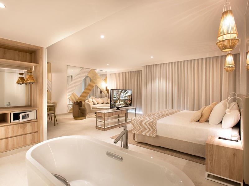 Modern eingerichtetes Hotelzimmer mit großzügigem Bett, freistehender Badewanne und warmem Licht.