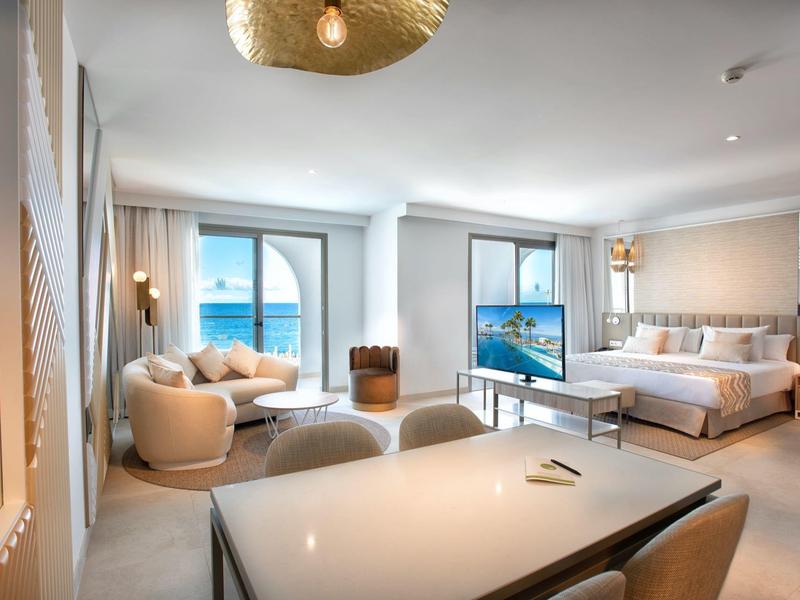 Helles Wohnzimmer mit großen Fenstern, cremefarbenen Möbeln und Blick auf das Meer.