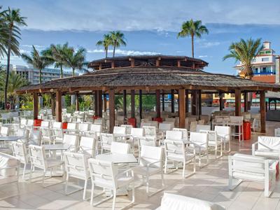 Open pavilion with white chairs surrounded by palm trees under a clear sky.