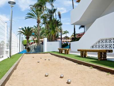 Outdoor area with bocce court, benches, and palm trees beside a white building.