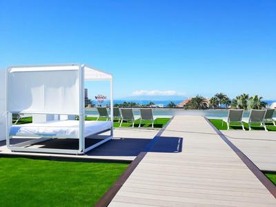 Area esterna moderna con lettini e letto a baldacchino vista mare sotto un cielo limpido.