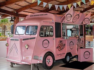 Pink food truck with decorations and branding inside a wooden-roofed indoor space.