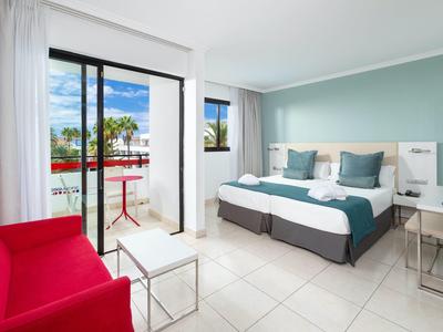 Camera d'hotel luminosa con letto matrimoniale, poltrona rossa e balcone con tavolo e sedia.