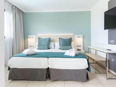 Camera d'albergo moderna con due letti singoli, cuscini turchesi e biancheria da letto bianca.