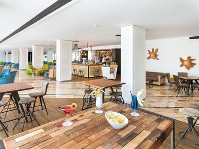 Lounge moderna dell'hotel con pavimenti in legno, sedie colorate e bar sullo sfondo.