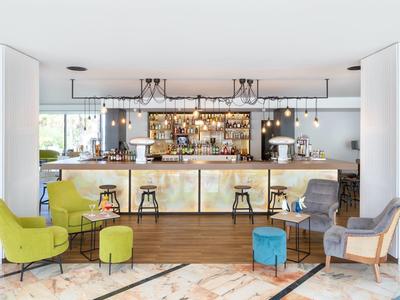 Area bar moderna con poltrone colorate e sgabelli in un interno d'hotel luminoso.