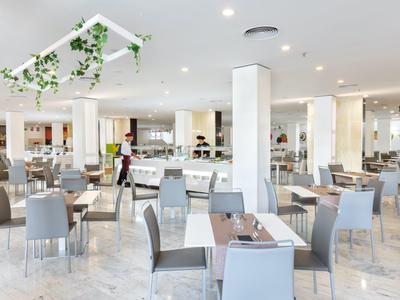 Ristorante dell'hotel moderno e luminoso con molti tavoli e sedie grigie, decorato con piante.