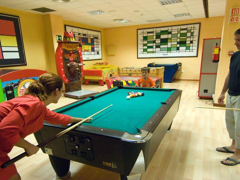 Due persone giocano a biliardo in una stanza luminosa con pareti gialle e arredamento moderno.