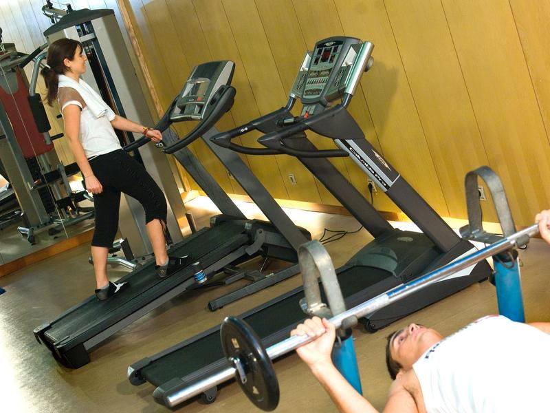 Persone che si allenano su tapis roulant e sollevano pesi in palestra.