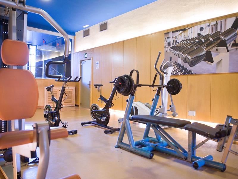 Palestra moderna con varie attrezzature e pavimento in legno chiaro.