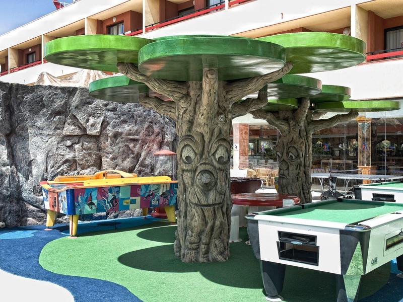 Cortile dell'hotel con tavoli da gioco e strutture ombreggianti a forma di albero.