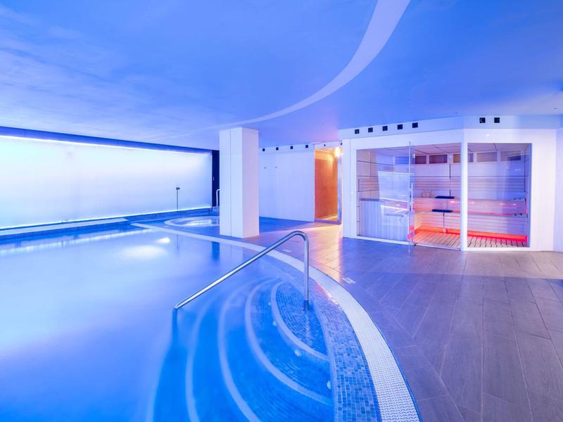 Una moderna area piscina interna con design curvo e vasca idromassaggio integrata.