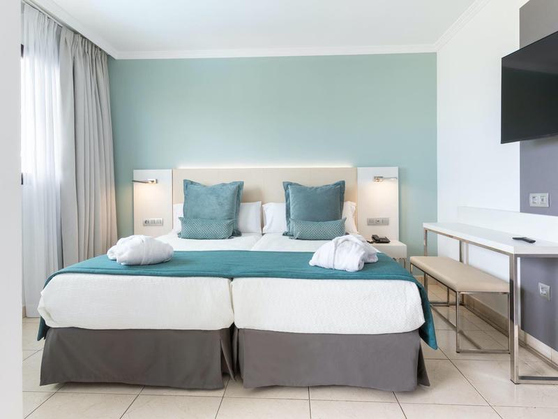 Camera d'albergo moderna con due letti singoli, cuscini turchesi e biancheria da letto bianca.