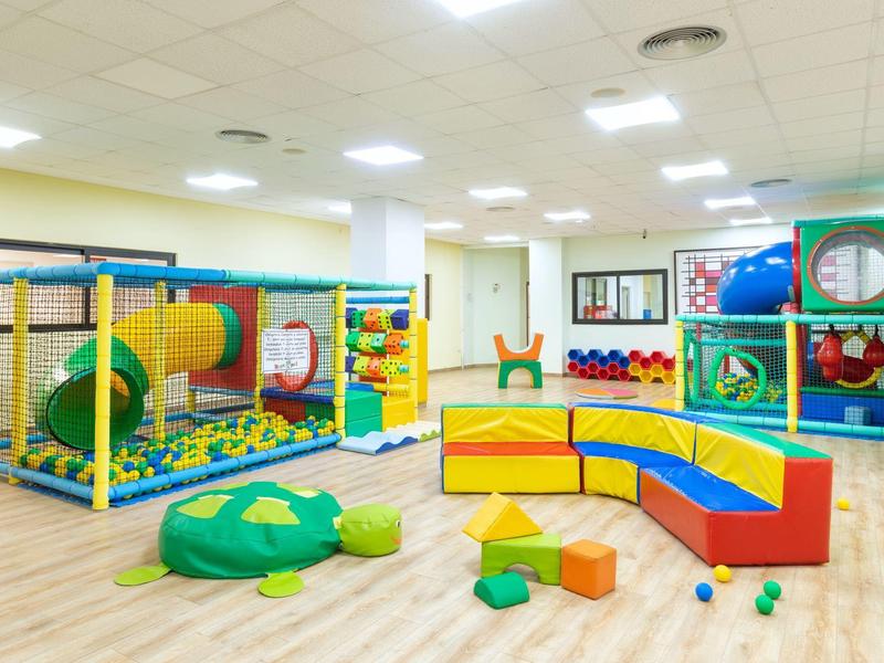 Sala giochi colorata per bambini con struttura arrampicata, scivolo e sedute morbide in uno spazio luminoso.