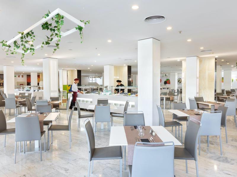 Ristorante dell'hotel moderno e luminoso con molti tavoli e sedie grigie, decorato con piante.