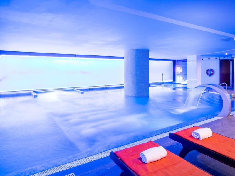 Piscina coperta con pareti blu, pilastro e lettini con asciugamani bianchi.