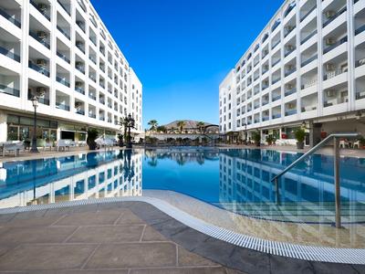 Großer Swimmingpool zwischen zwei weißen Hotelgebäuden unter klarem blauem Himmel.