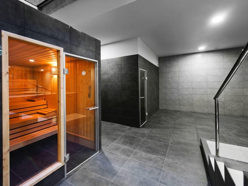 Moderne Sauna mit Holzinterieur, Glasfront und grauen Kacheln im angrenzenden Bereich.