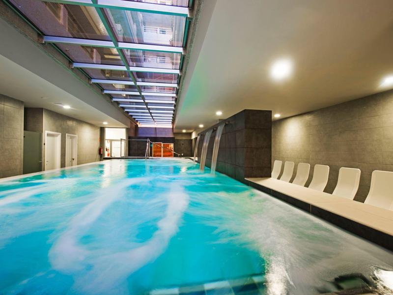 Moderner Innenpool mit blauem Wasser, Whirlpoolbereich und weißen Liegestühlen an der Seite.