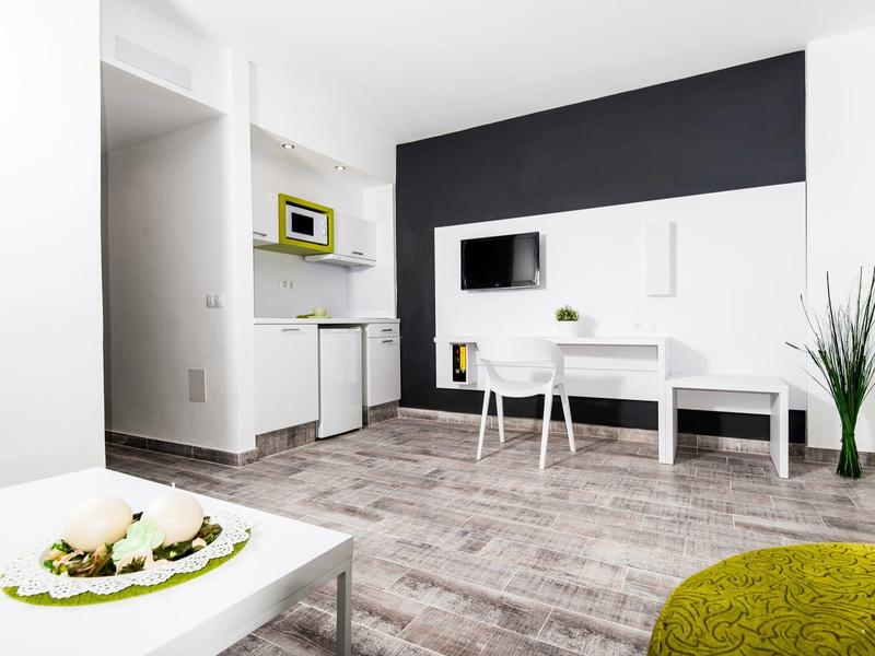 Moderner, heller Wohnraum mit weißem Mobiliar, grauem Parkettboden und grünen Akzenten.