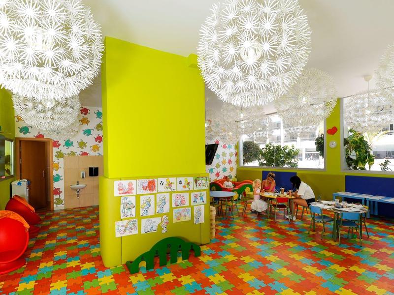 Bunter Kindergartenraum mit grün gestrichenen Wänden, gemustertem Boden und Spielzeug.