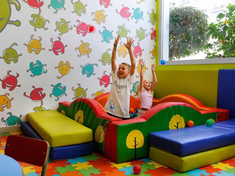 Bunte Kinderspielecke mit gepolsterten Kletterelementen, buntem Boden und fröhlicher Wanddekoration.