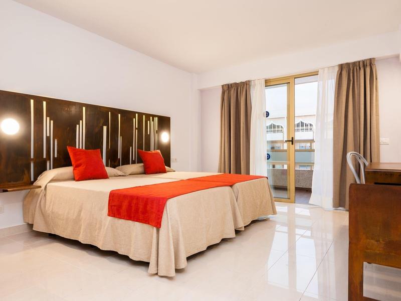 Modernes Schlafzimmer mit Doppelbett, roten Akzenten und Balkon mit Glasfenstern.