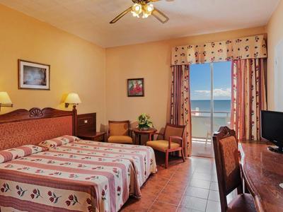 Habitación de hotel con dos camas, escritorio y vista al mar desde un balcón.
