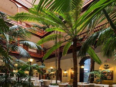 Patio de hotel con palmeras verdes y asientos blancos bajo luz natural.