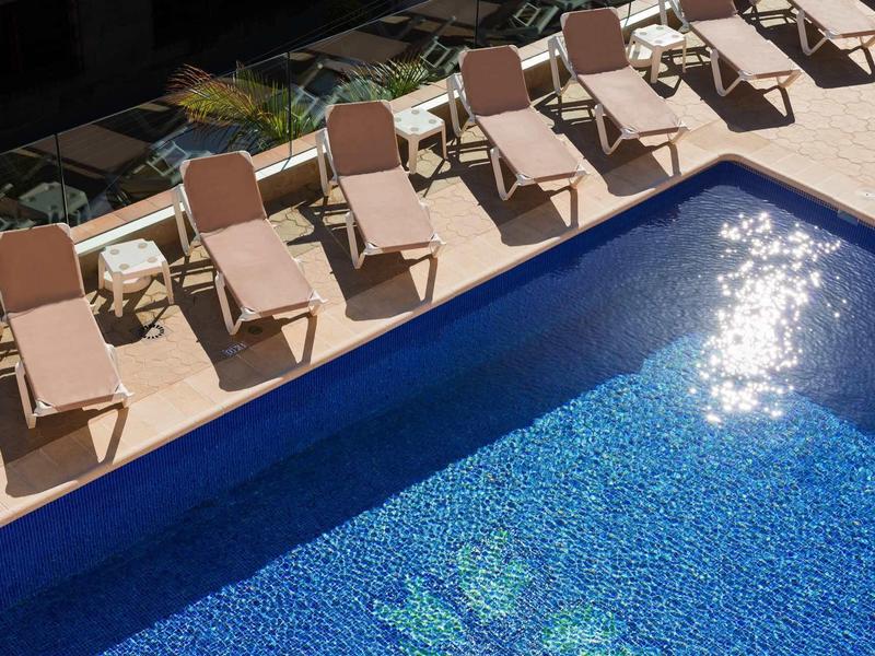 Blauer Pool mit reflektierendem Sonnenlicht und einer Reihe von neun beigen Liegestühlen am Rand.