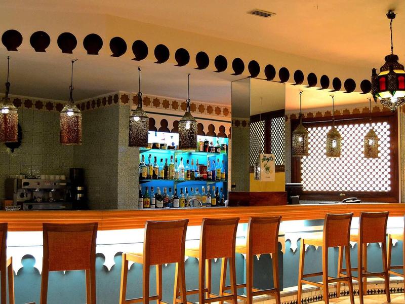 Moderner Barbereich mit hölzernen Barhockern, beleuchteter Theke und dekorativen Lampen an der Decke.