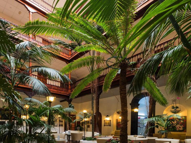 Innenhof mit Palmen, weißen Sesseln und Tischen, umgeben von mehrstöckigem Gebäude.