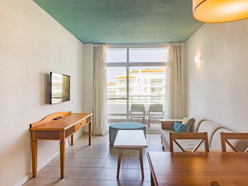 Jasny pokój z biurkiem, telewizorem, stołem i krzesłami przy dużym oknie