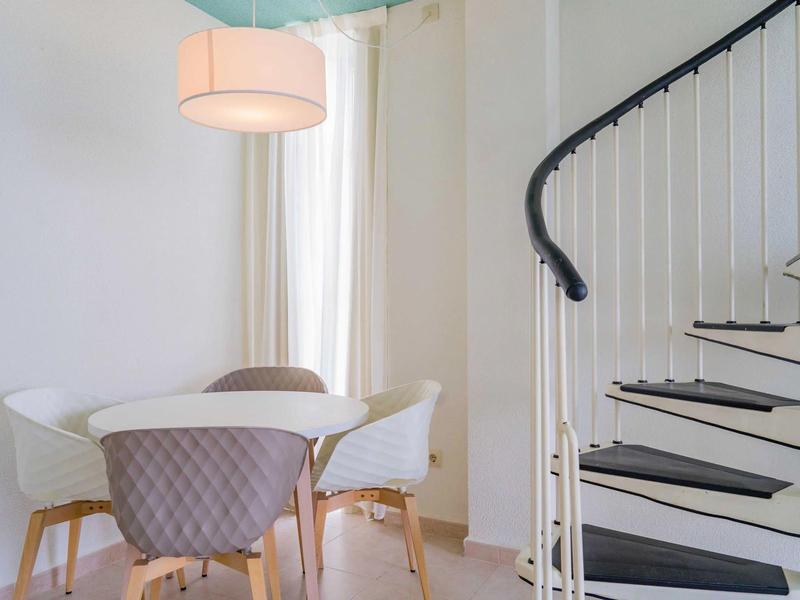 Nowoczesna jadalnia z okrągłym stołem, tapicerowanymi krzesłami i białą spiralną klatką schodową.