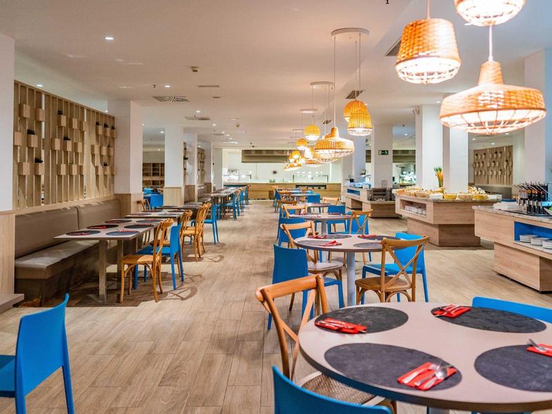 Nowoczesna część restauracyjna z drewnianą podłogą, niebieskimi krzesłami i wiszącymi lampami.